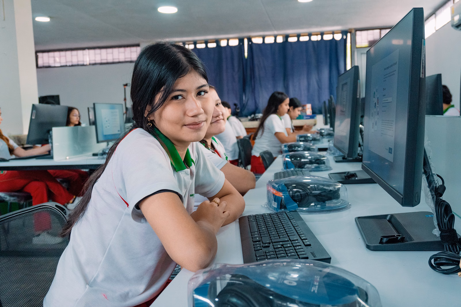 Una estudiante sonríe frente a su computadora en un aula